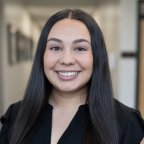 Megan White, with long dark hair and a black top, smiles at the camera.