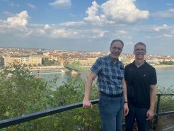 Luke Perry and Faculty Host Dr Karoly Pinter in Budapest, with water and buildings behind them.