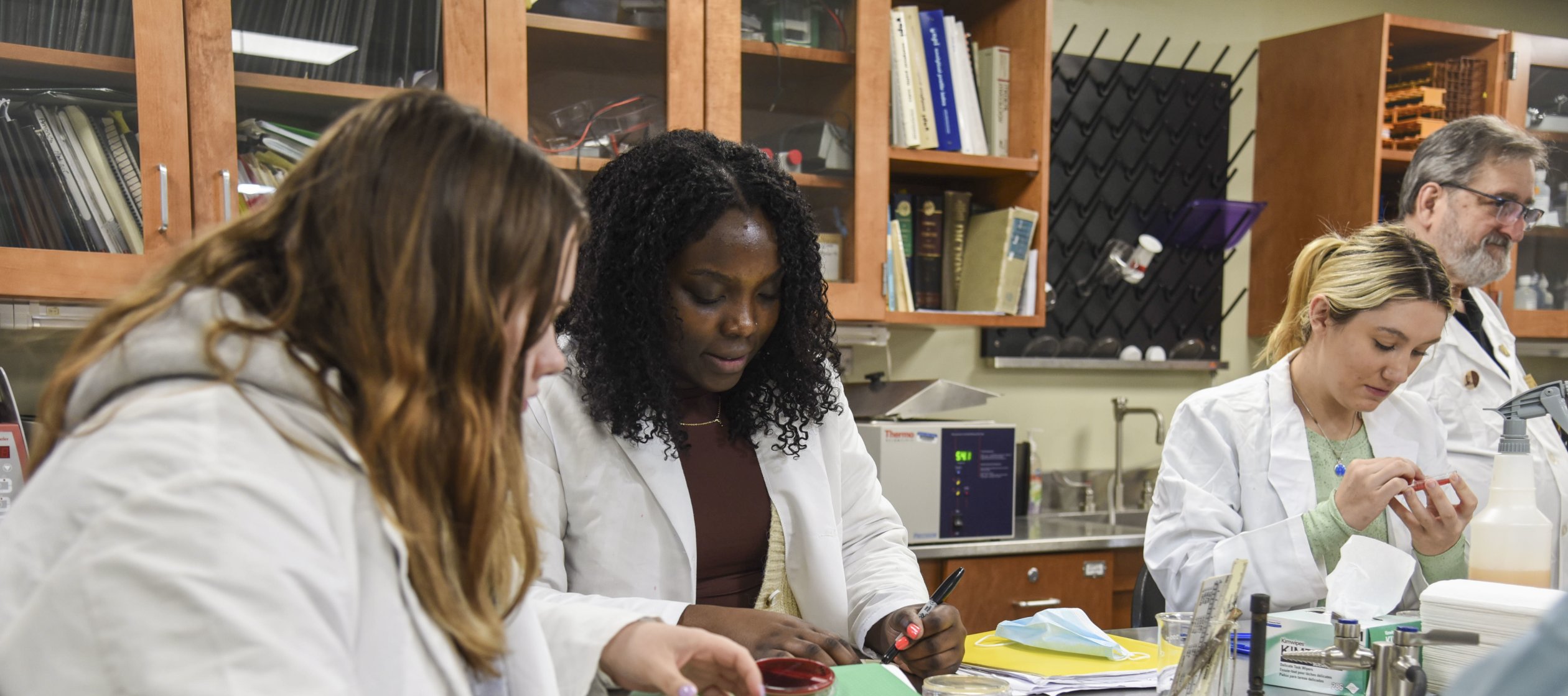 Students in white lab coats work in the microbiology lab.