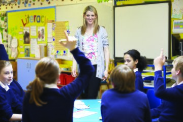 Teacher in a classroom with students raising their hands.