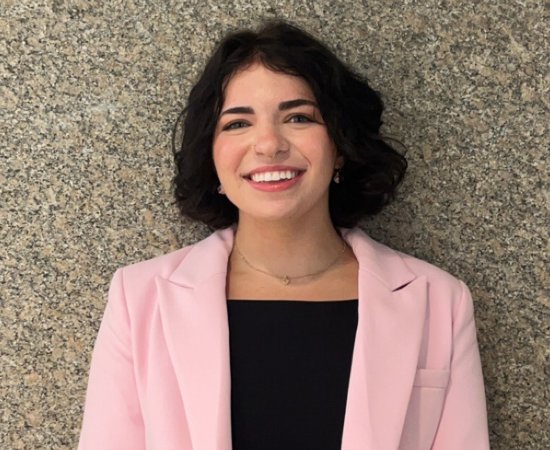 Grace VanEtten '27 in black top and pink blazer, stands against a stone wall.