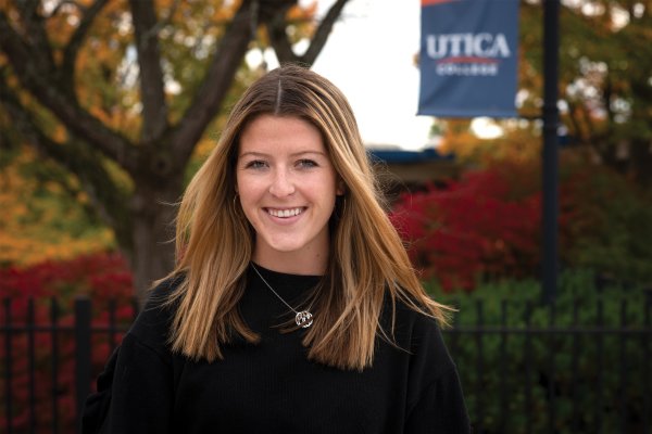 Jackie Rueckert stands in front of Utica College banner.