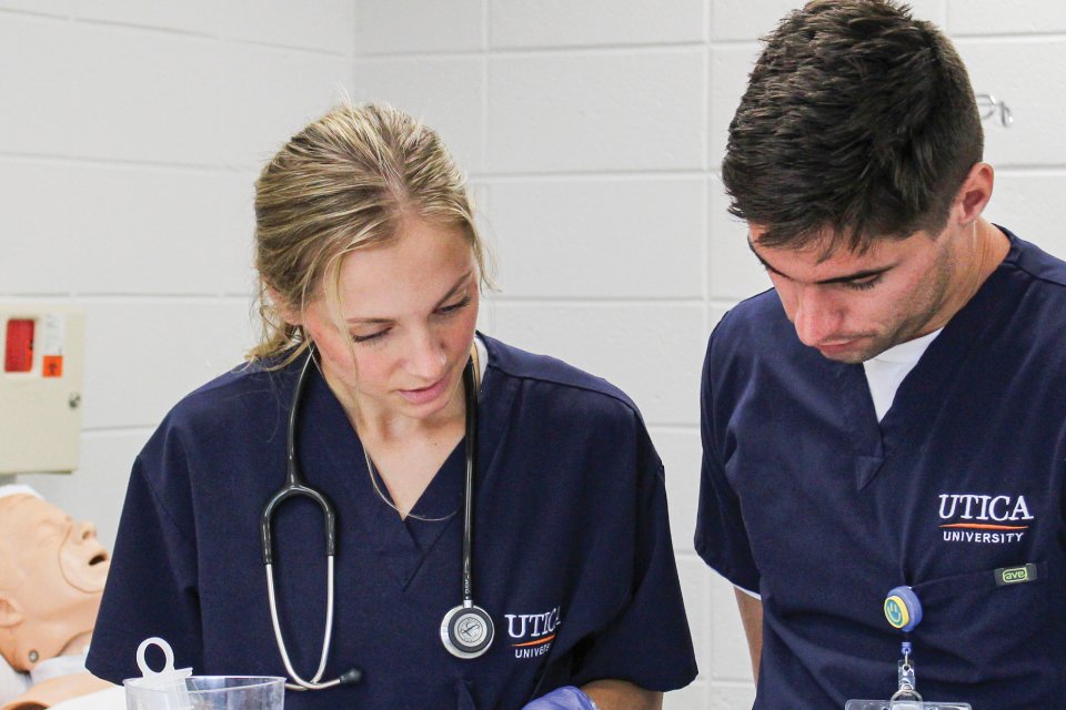 Nursing students in scrubs, look over paperwork near a mock-patient.